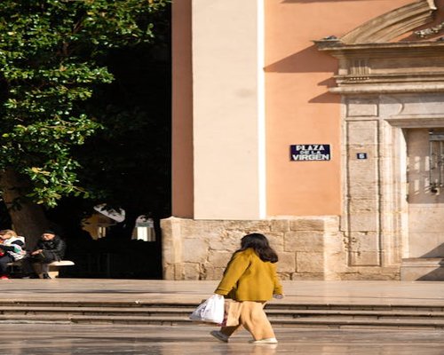 Woman enjoying a sunny walk in a vibrant Spanish plaza carrying light groceries
